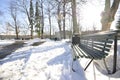 Snow-covered park with melted footpath. Beautiful winter landscape in the city. Decorative streetlamps and park benches in a row