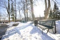 Snow-covered park with melted footpath. Beautiful winter landscape in the city. Decorative streetlamps and park benches in a row