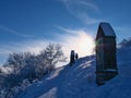 Snow-covered path along crossroad on KornbÃÂ¼hl hill with stone shrines in bright afternoon sun in winter near Burladingen.