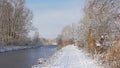 Snow covered path along a frozen creek with bare winter trees and shrubs on the sides Royalty Free Stock Photo