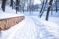 Snow-covered pathway beside a stone wall, lined with trees, creates a serene winter scene, inviting exploration and Royalty Free Stock Photo
