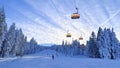 The snow-covered piste for skiers and snowboarders, equipped with snow cannons and lampposts, runs under a four-seat chairlift thr