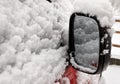 Snow covered red car parked outside, rear view mirror, winter transport challenge