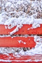 Snow covered red wooden bench, snow covered bushes in winter park Royalty Free Stock Photo