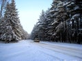A snow-covered road runs through a winter forest, along which a lonely white car is driving. Royalty Free Stock Photo