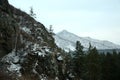 Snow-covered rocky slope of a high mountain with rare coniferous trees overlooking a beautiful valley in the mountains on a cloudy Royalty Free Stock Photo