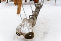 A snow-covered swing in the old style in the form of a log suspended from chains.