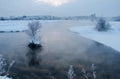 Snow-covered winter white trees on the shore of the lake in the early morning, reflections of the sky in the dark water Royalty Free Stock Photo