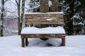 A snow-covered wooden bench in a winter park. Next to the bench is a round trash can Royalty Free Stock Photo