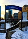 Snow covering urban landscape of Chicago Loop after winter storm, while sun sets over entrance to the riverwalk at Chicago River.