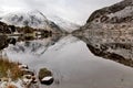 Snow dusted Glyder mountains rising into the clouds reflected in Llyn Ogwen