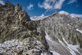 Snow dusted mountain peaks tower against a bright blue sky, with rocky outcrops and steep inclines