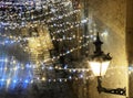 View from window glass on evening Christmas street , yellow lantern lamp on house wall illumination and light blurred on wet pavem Royalty Free Stock Photo