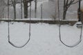 Snow falling on empty swings in a deserted park. It is cold and eerie and dingy.