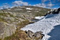 Snow field and rocks with lichens in early summer in the Norwegian mountains, a lake of melted snow, near Bergen. Blue sky. Royalty Free Stock Photo