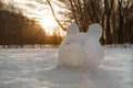 A snow figure in the shape of a bear s head, made by a man. Against the backdrop of a snowy field at sunset