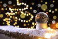 Snow globe and blurred Christmas lights on background. Winter decor Royalty Free Stock Photo