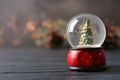 Snow globe with Christmas tree on grey wooden table against festive lights Royalty Free Stock Photo