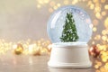 Snow globe with Christmas tree on marble table, space for text. Bokeh effect