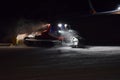 A snow groomer compacting ski runs at night