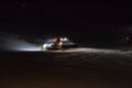 A snow groomer compacting ski runs at night