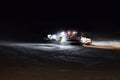 A snow groomer compacting ski runs at night