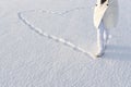 Snow heart made by footsteps. Anonymous woman in white winter coat, walks on snow in snow boots. Royalty Free Stock Photo