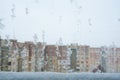 Snow and ice on the window against the background of the city during the winter day. Close up snowy glass on the blurred