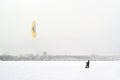 Snowkiter rides on the ice of a city water body during a snowfall