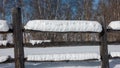 Snow lies in thick layers on an old unpainted log fence