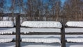 Snow lies in thick layers on an unpainted log fence.