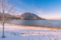 Snow on Okanagan Beach with aspen tree and view of Okanagan Lake and distant mountains at sunset Royalty Free Stock Photo