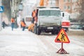 Snow-plow remove snow from the city street.Warning road sign.Winter service vehicle snow blower work.Cleaning snowy