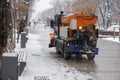 Snow plow is sprincling salt or de-icing chemicals on pavement in city. Cleaning service. Frost winter season.