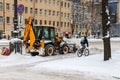 The snow-removing machine clears the snow from the road. One bicyclist is riding on a snow-covered road