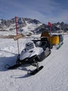 Snow resque mobile in italian Dolomites parked on ski slope - white mountains surrounding and groomer machine