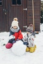 Snow time, games in the snow. Cute Caucasian children brother and sister make a snowman in the yard of their house. Fun during Royalty Free Stock Photo