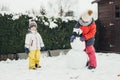 Snow time, games in the snow. Winter holidays. Cute Caucasian children brother and sister make a snowman in the yard of their Royalty Free Stock Photo