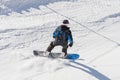 Snowboarder in a black suit in a helmet and with a backpack on his back rides along a mountain track on a sunny day