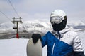 Snowboarder with a board in his hand stands on the top of the mountain of a ski resort amid the ski lift