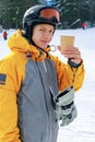 The snowboarder drinks hot coffee. A young guy of Caucasian ethnicity is holding a paper cup with a hot drink Royalty Free Stock Photo