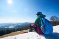 Snowboarder female resting on snowy summit enjoying view on background of blue sky and mountains.
