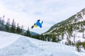 Snowboarder freerider jumping from a snow ramp in the sun on a background of forest and mountains