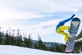 Snowboarder freerider jumping from a snow ramp in the sun on a background of forest and mountains