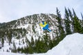 Snowboarder freerider jumping from a snow ramp in the sun on a background of forest and mountains