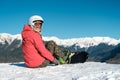Snowboarder girl sits with board at the ski slope in mountains