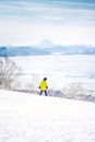 Snowboarder girl in yellow jacket riding down the hill in front of snowy mountains