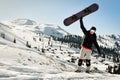 Snowboarder holding his snowboard over head in ski resort excited on holiday vacation solo