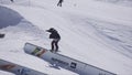 Snowboarder make backslide on rail on ski resort. Sunny day. Mountains. People.