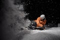 Snowboarder in orange jacket riding on a snowy hill at night